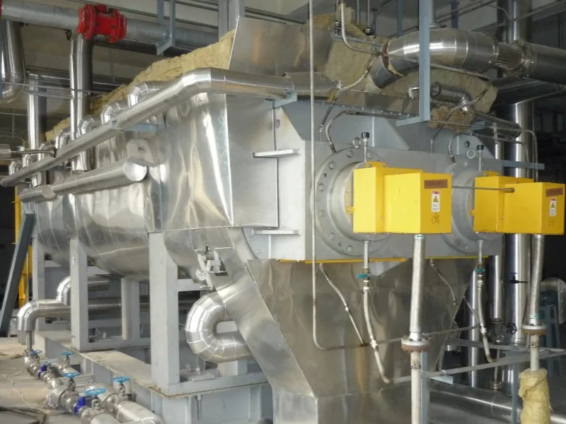 Stainless steel paddle dryer installed with process piping and a yellow drive guard
